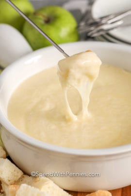 Cheese fondue in a white Bowl being dipped with bread from a fondue skewer