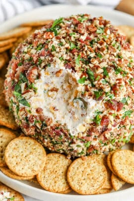 close up of Classic Cheese Ball with a bite taken out and crackers surrounding it on a plate