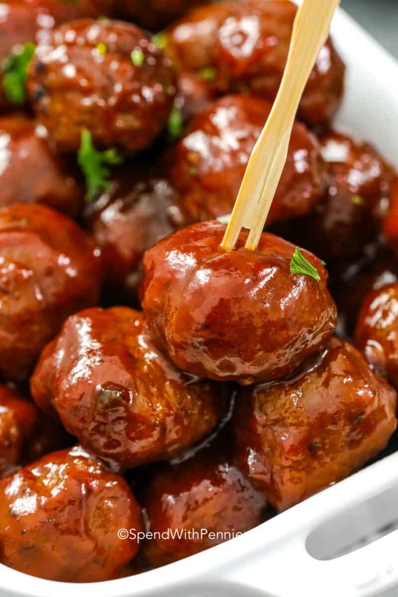grape jelly meatballs in a serving dish with a cocktail pick