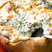 taking a spoonful of Hot Spinach and Artichoke Dip in a bread bowl