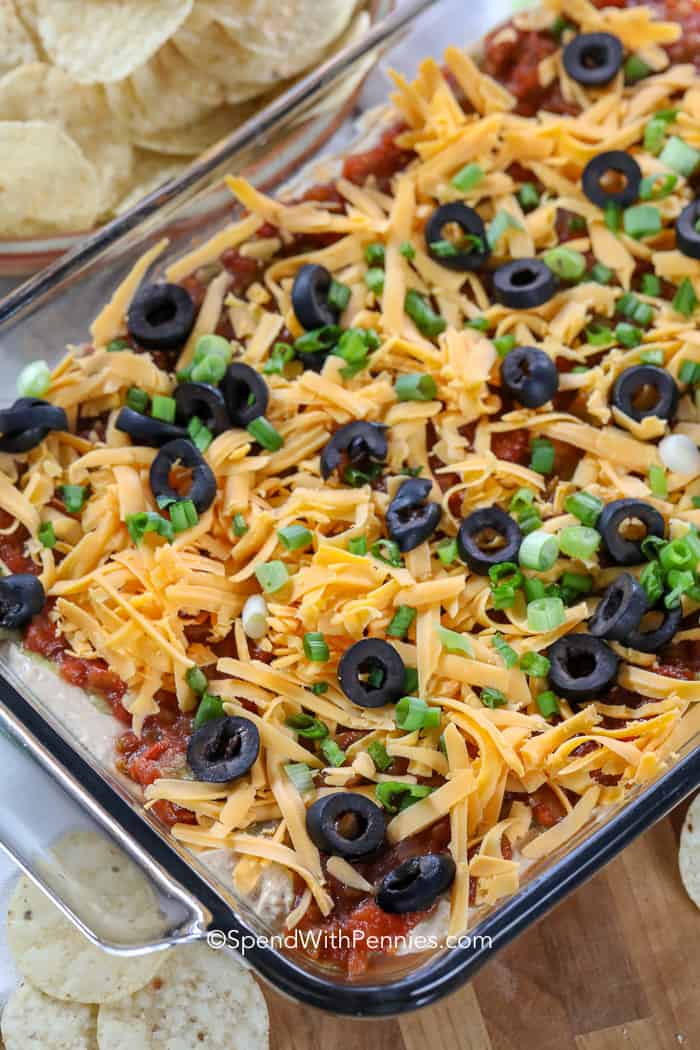 7 Layer Dip in a clear dish with tortilla chips in the background