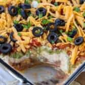 7 Layer Dip in a casserole dish with a scoop taken out